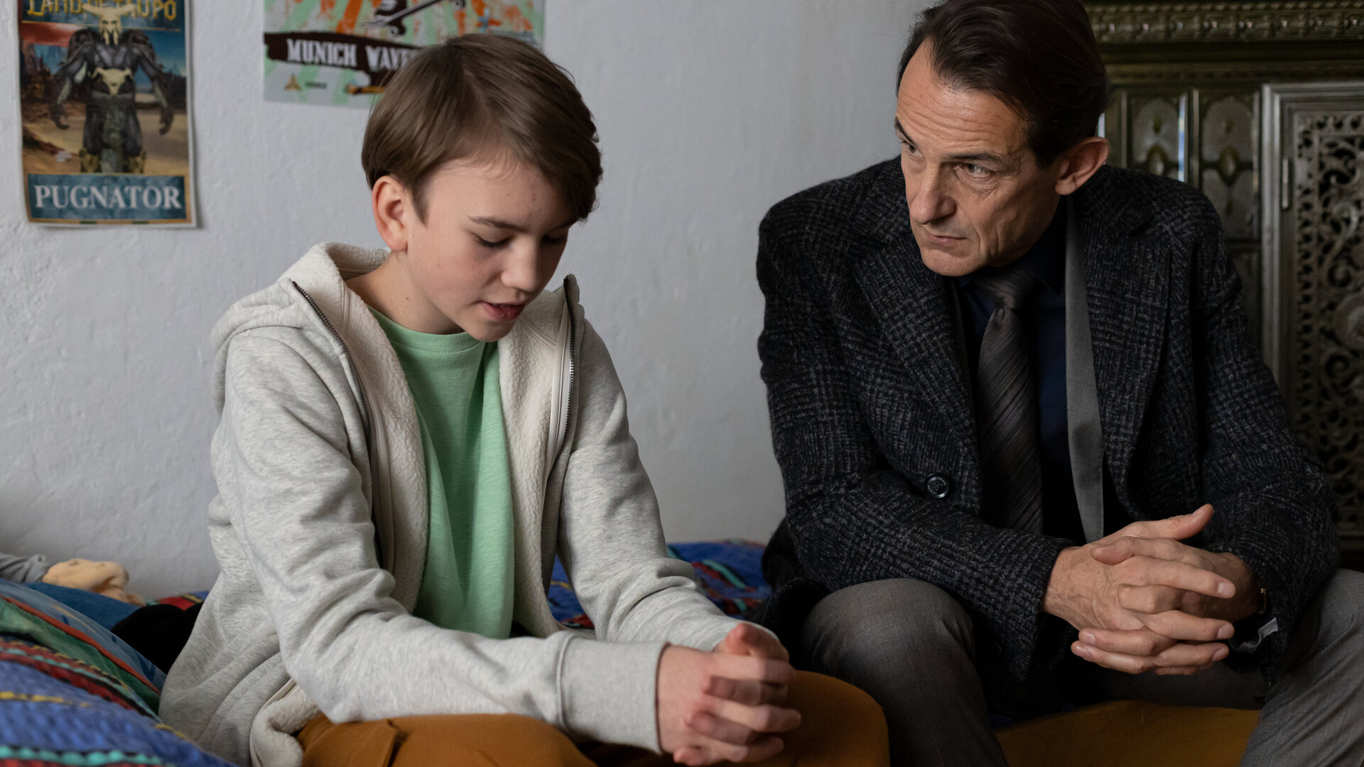 "Letzte Spur Berlin - Das weiße Rauschen": Henri Schwab (Ari Kurecki) sitzt auf seinem Bett mit gesenktem Blick und zusammengefalteten Händen. Er spricht mit Oliver Radek (Hans-Werner Meyer), der neben ihm auf dem Bett sitzt und mitleidig ihn anschaut.