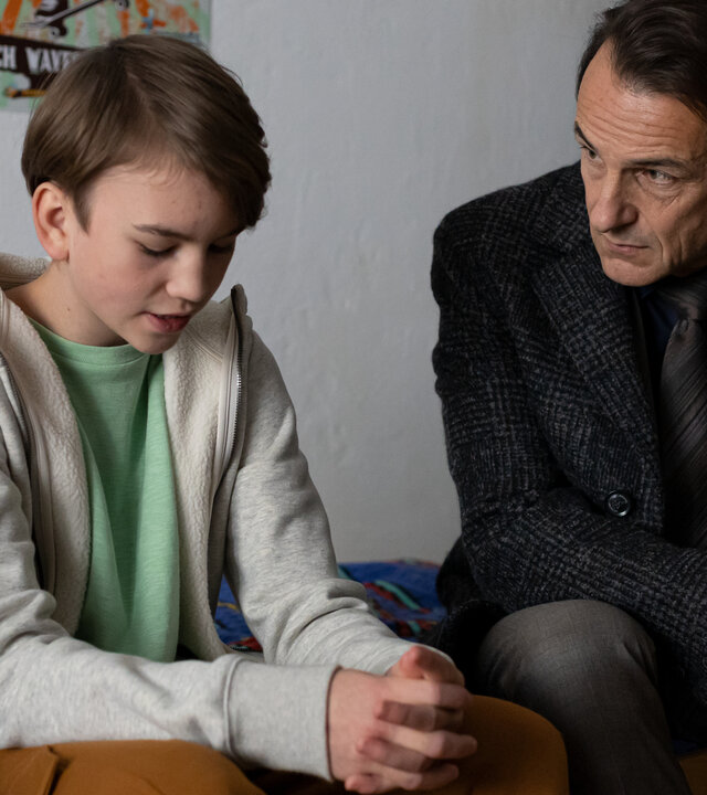 "Letzte Spur Berlin - Das weiße Rauschen": Henri Schwab (Ari Kurecki) sitzt auf seinem Bett mit gesenktem Blick und zusammengefalteten Händen. Er spricht mit Oliver Radek (Hans-Werner Meyer), der neben ihm auf dem Bett sitzt und mitleidig ihn anschaut.