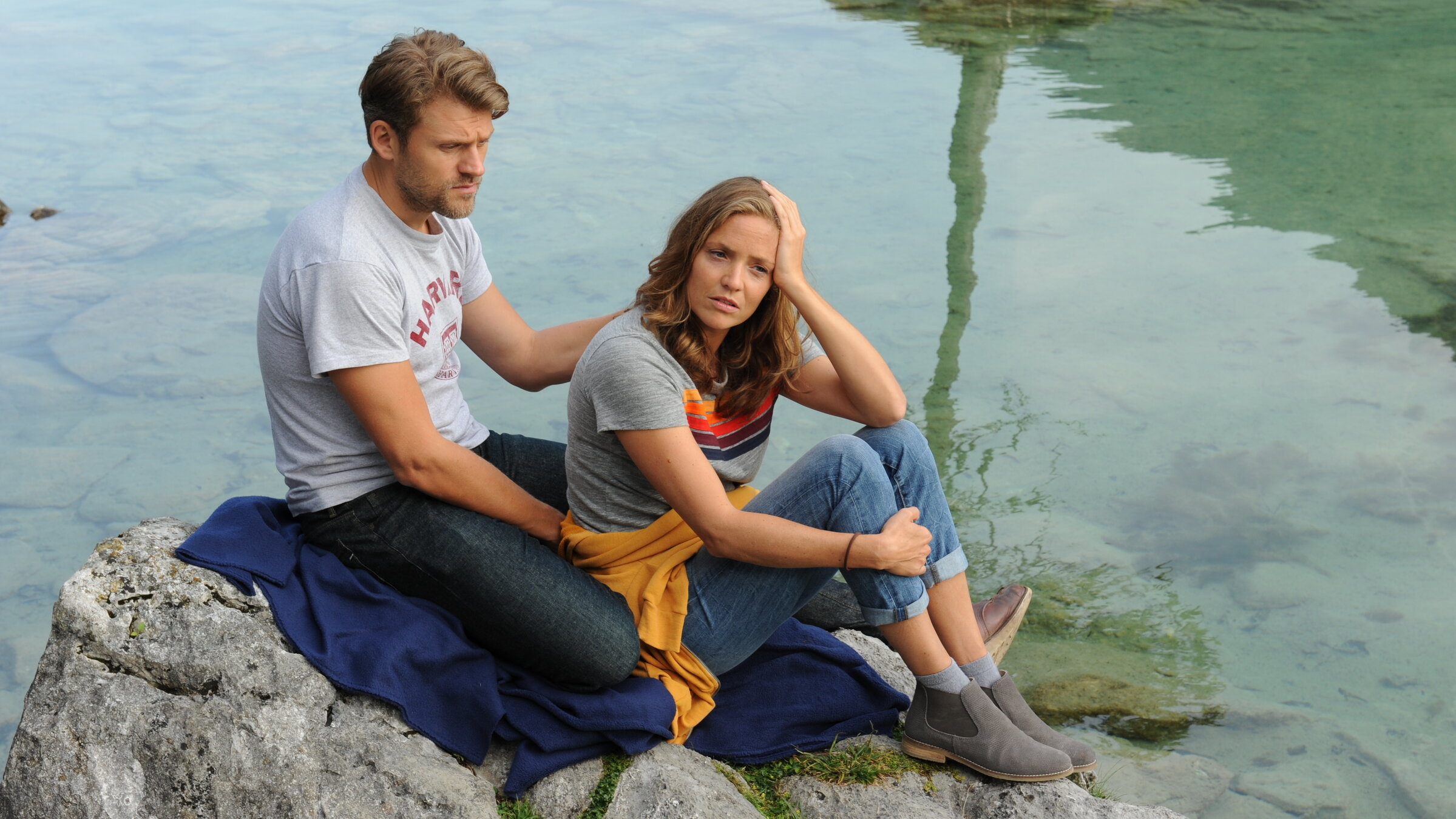 "Lena Lorenz - Wunsch und Wirklichkeit": Quirin Pankofer (Jens Atzorn) und Lena Lorenz (Patricia Aulitzky) sitzen nachdenklich auf einem Felsen, der in einen See hineinragt.