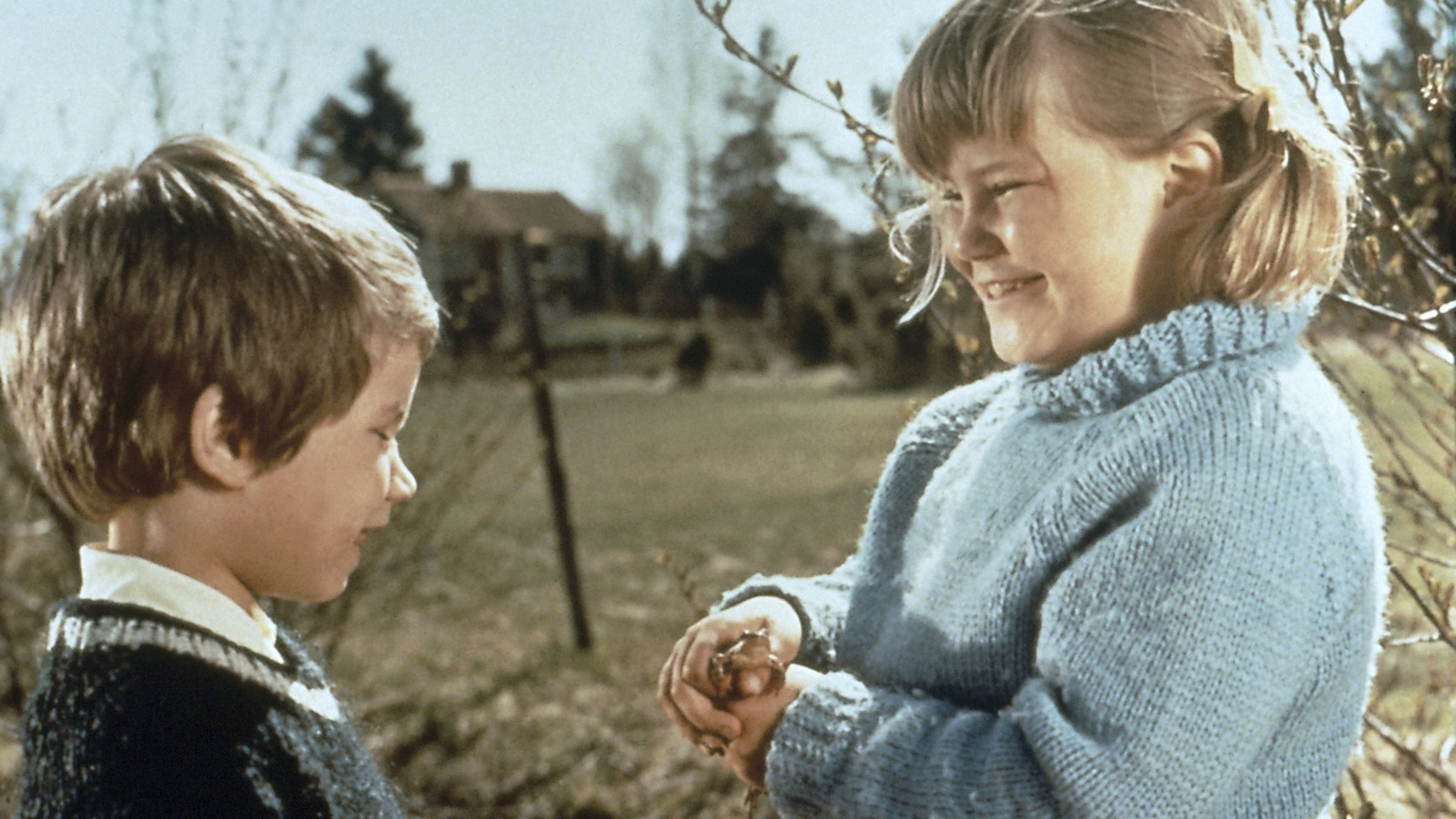 "Ferien auf Saltkrokan": Stina (Kristina Jämtmark) steht lächelnd, mit einem Frosch in beiden Händen, vor Tjorven (Maria Johansson), die ebenfalls lächelnd, auf den Frosch schaut.
