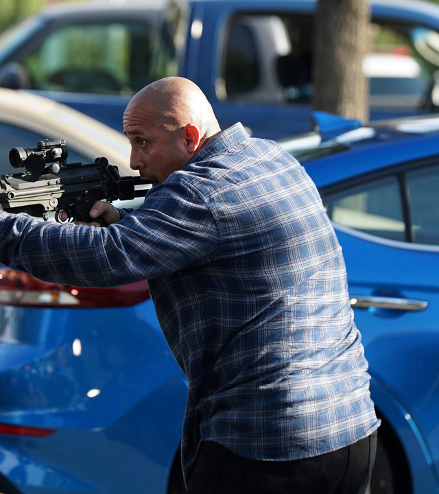 "The Rookie - Der Tausch": Außenaufnahme auf einem Parkplatz. Ein kahlköpfiger Mann hält mit beiden Händen ein Gewehr abschussbereit nach vorne.