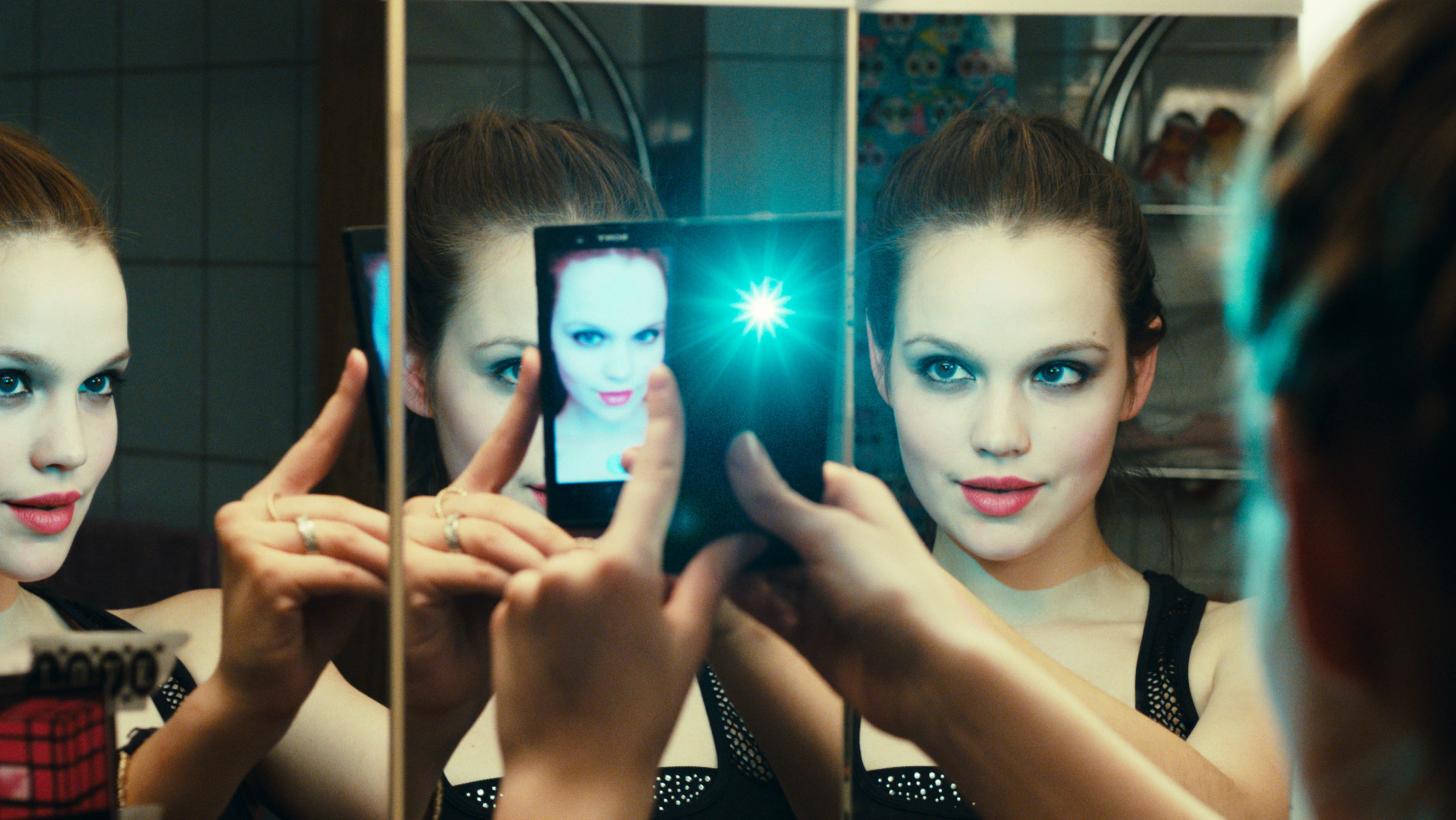 "LenaLove": Lena (Emilia Schüle) macht ein Selfie vor einem Spiegel, in dem man sie drei Mal sieht.