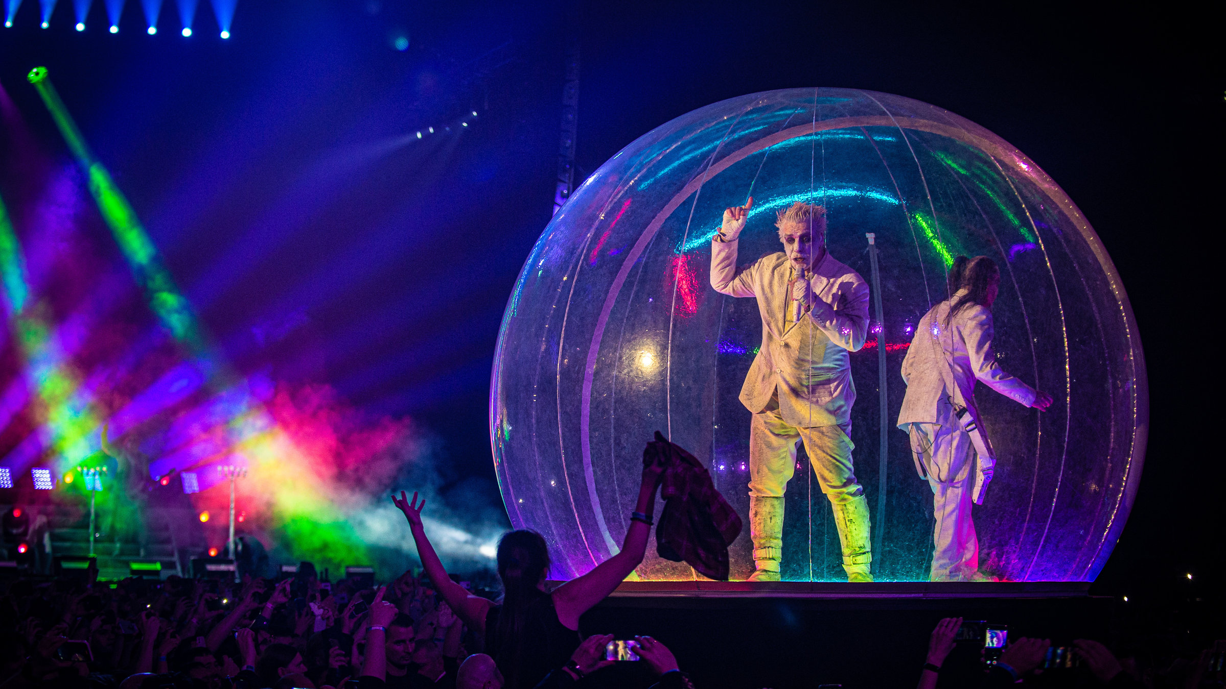 "LINDEMANN: Live in Moscow": Zwei Männer in weißen Anzügen stehen auf der Bühne. Sie sie sind in einem durchsichtigen Ballon, der an eine Seifenblase erinnert und werden von bunten Scheinwerfern angestrahlt.