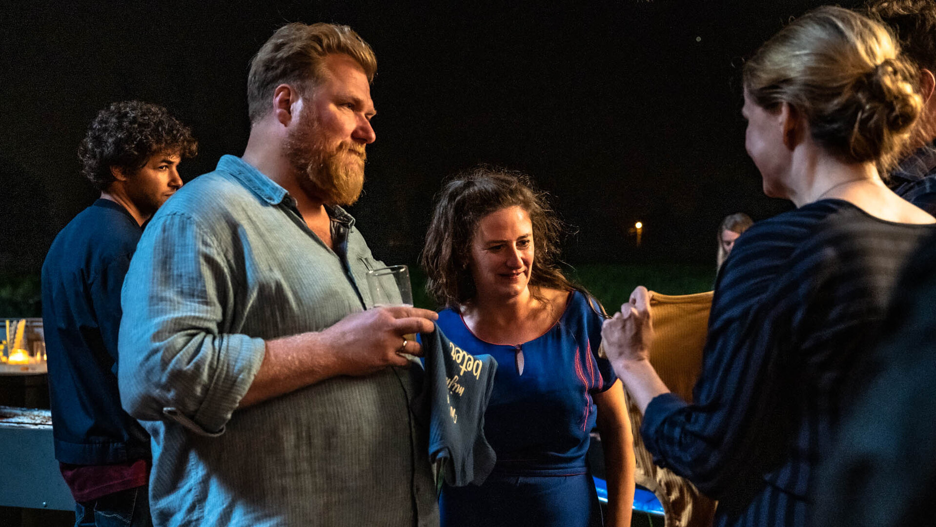 "The Club - Der Baby-Bingo-Club": Lies (Julie Mahieu) zeigt Bert (Dominique Van Malder) und Kirstie (Janne Desmet) ein kleines Kindertshirt. Bert und Kirstie blicken mit Unbehagen zu ihr.