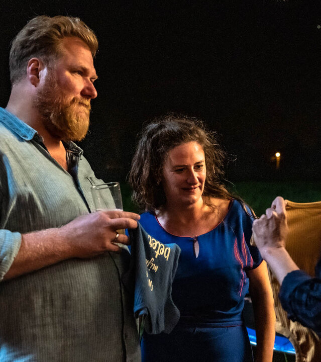 "The Club - Der Baby-Bingo-Club": Lies (Julie Mahieu) zeigt Bert (Dominique Van Malder) und Kirstie (Janne Desmet) ein kleines Kindertshirt. Bert und Kirstie blicken mit Unbehagen zu ihr.