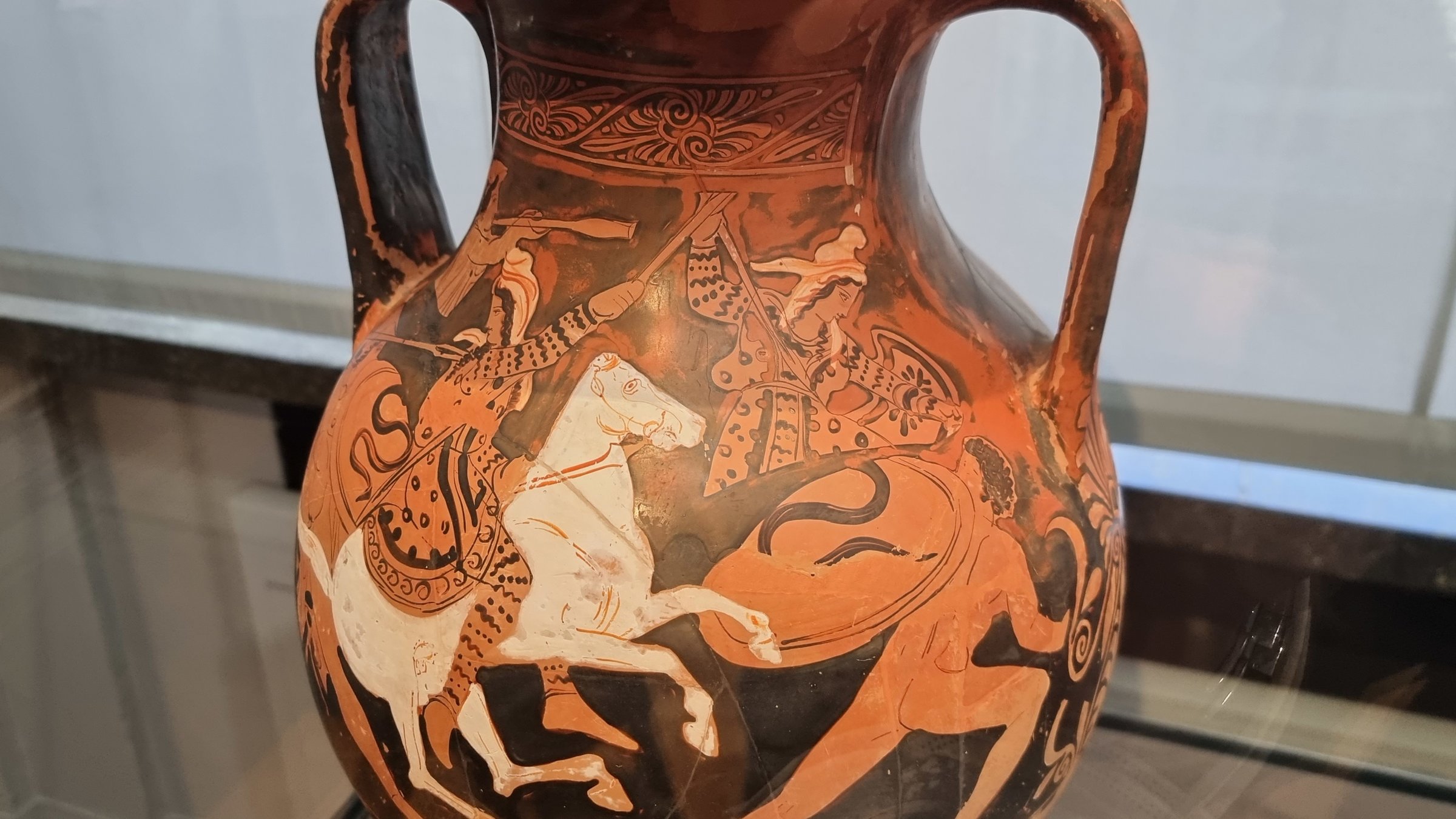 "Terra X: Ungelöste Fälle der Archäologie - Rätselhafte Amazonen": Schwarz, weiß, rot und ockerfarbige Darstellung auf einer antiken Vase. Das Bild zeigt zwei Reiterinnen, die gegen einen unbekleideten Schildträger kämpfen.
