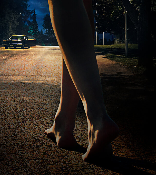 "It Follows": Jay (Maika Monroe) steht im Hintergrund nachts auf einer einsamen Straße. Im Vordergrund sind zwei nackte Füße zu sehen, die auf sie zugehen.