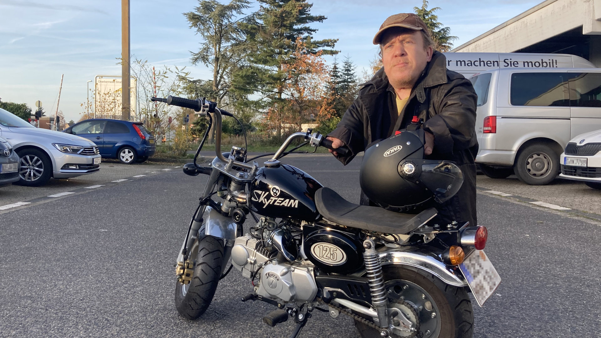 "einfach Mensch - Ich entscheide, was ich kann!": Martin Müller in schwarzer Jacke steht auf einem Parkplatz vor seinem Motorrad, am Arm den Helm.