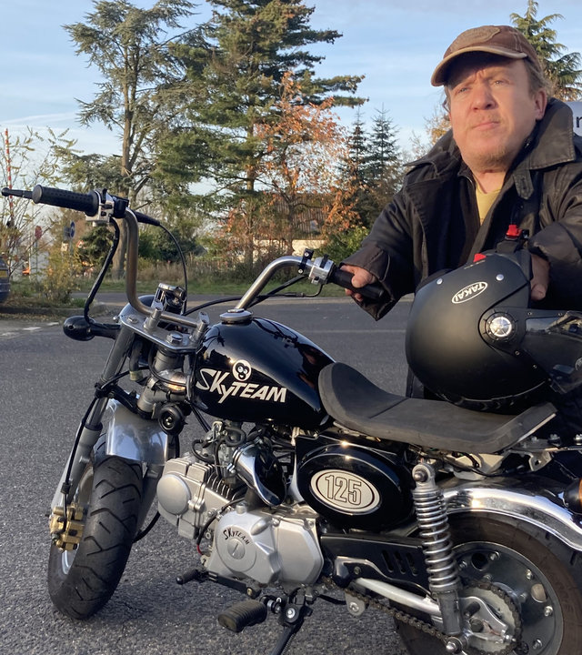 "einfach Mensch - Ich entscheide, was ich kann!": Martin Müller in schwarzer Jacke steht auf einem Parkplatz vor seinem Motorrad, am Arm den Helm.