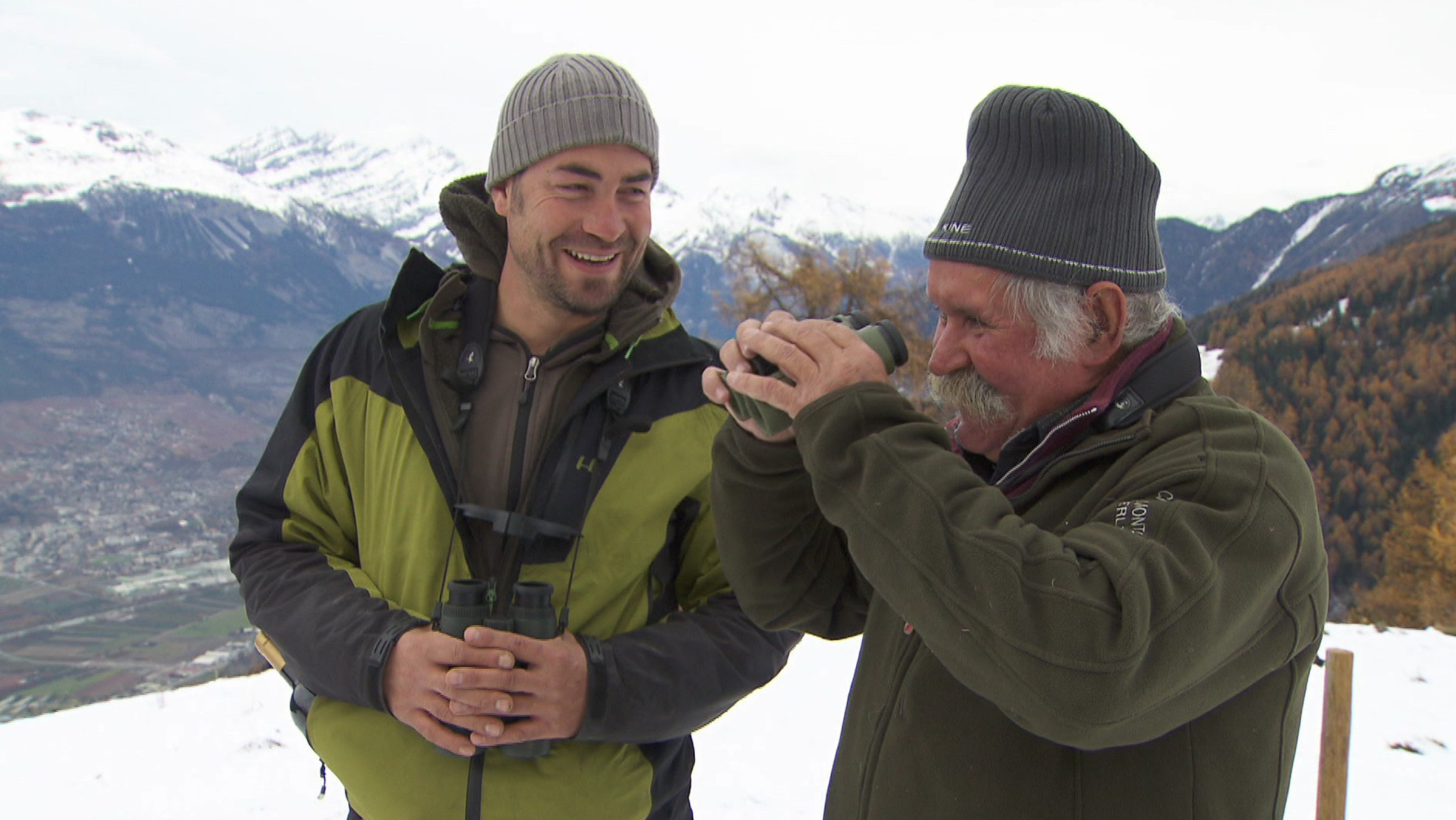 "Der listige Jäger aus dem Wallis": Zwei Personen mit Ferngläsern in einer winterlichen Berglandschaft