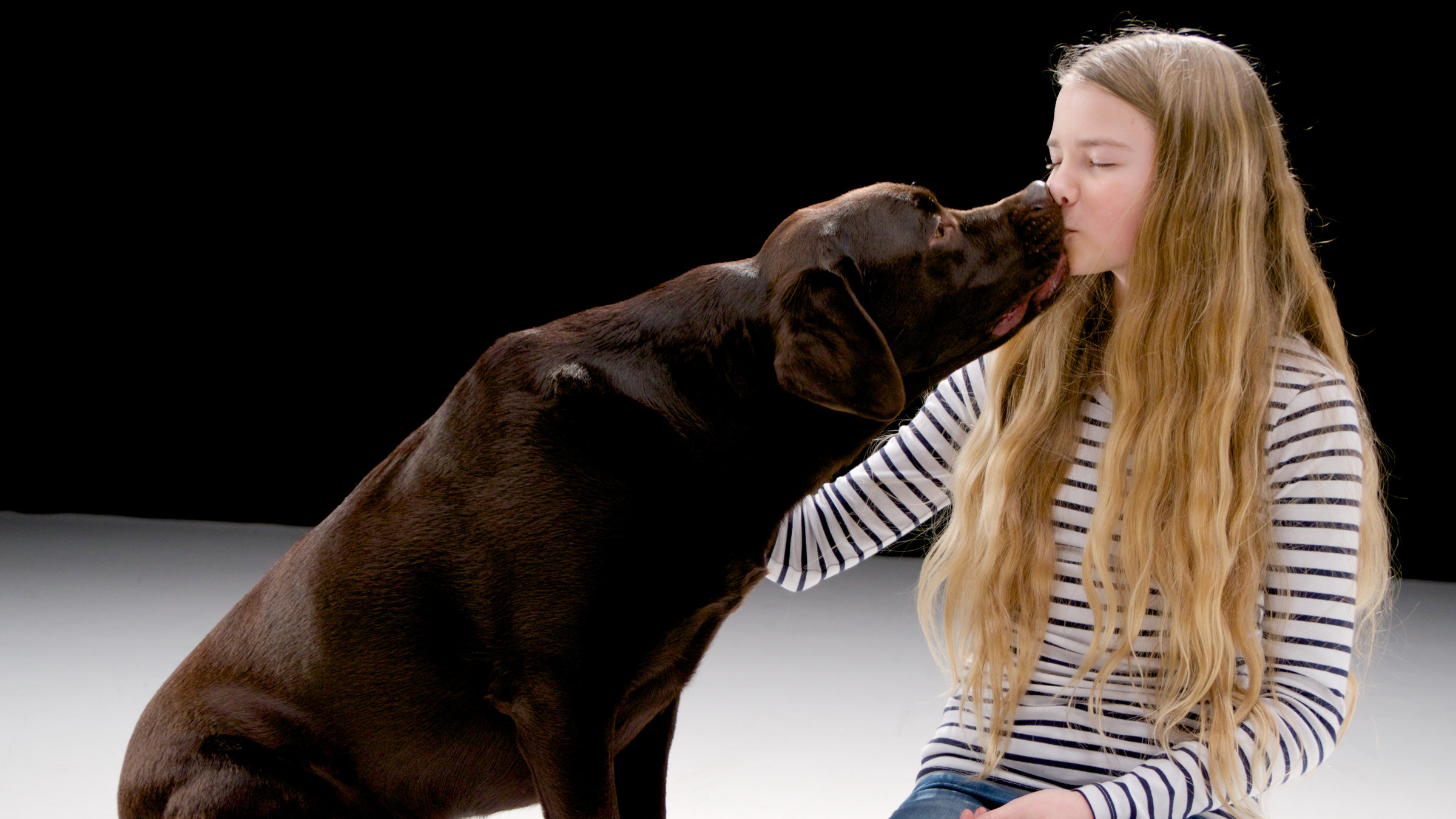"Urvertrauen - das Band zwischen Mensch und Hund": Ein brauner Labrador küsst ein junges Mädchen.