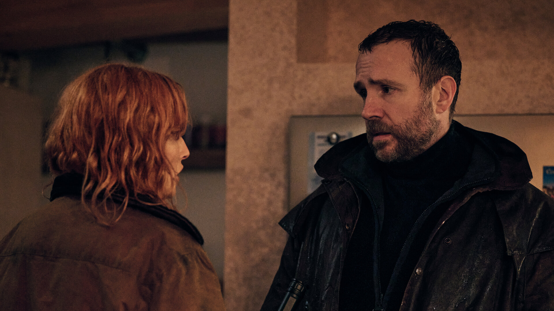 "Under Salt Marsh - Tod in den Salzwiesen - Die Flut": Jackie (Kelly Reilly) und Eric (Rafe Spall) stehen sich in einem Wohnraum gegenÃ¼ber. Sie hÃ¤lt eine nicht eingeschaltete Taschenlampe in der Hand.