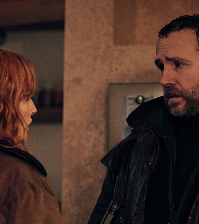 "Under Salt Marsh - Tod in den Salzwiesen - Die Flut": Jackie (Kelly Reilly) und Eric (Rafe Spall) stehen sich in einem Wohnraum gegenÃ¼ber. Sie hÃ¤lt eine nicht eingeschaltete Taschenlampe in der Hand.