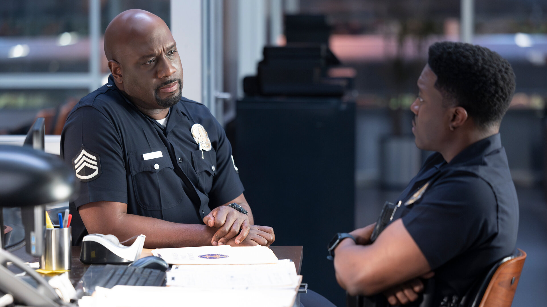 "The Rookie - Trainingstag": Officer Grey (Richard T. Jones) sitzt schräg gegenüber von Officer Aaron Thorsen (Tru Valentino) an einem Schreibtisch und blickt ihn ernst an.