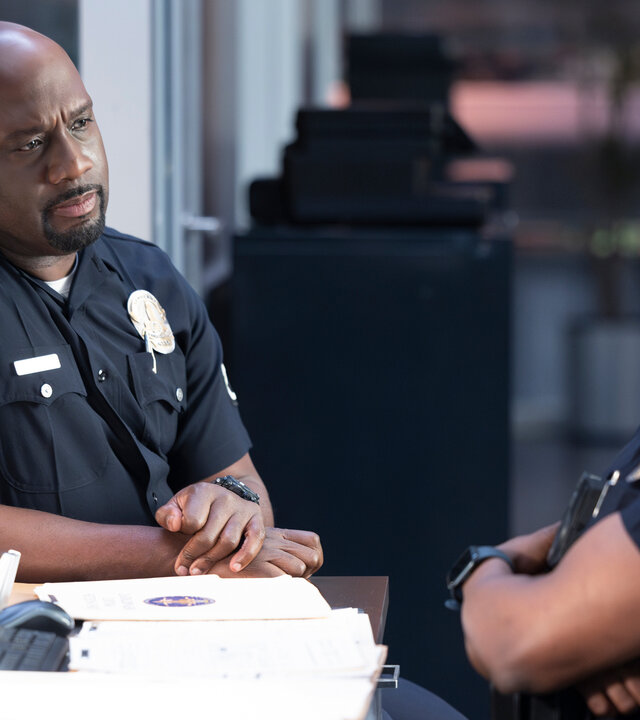 "The Rookie - Trainingstag": Officer Grey (Richard T. Jones) sitzt schräg gegenüber von Officer Aaron Thorsen (Tru Valentino) an einem Schreibtisch und blickt ihn ernst an.