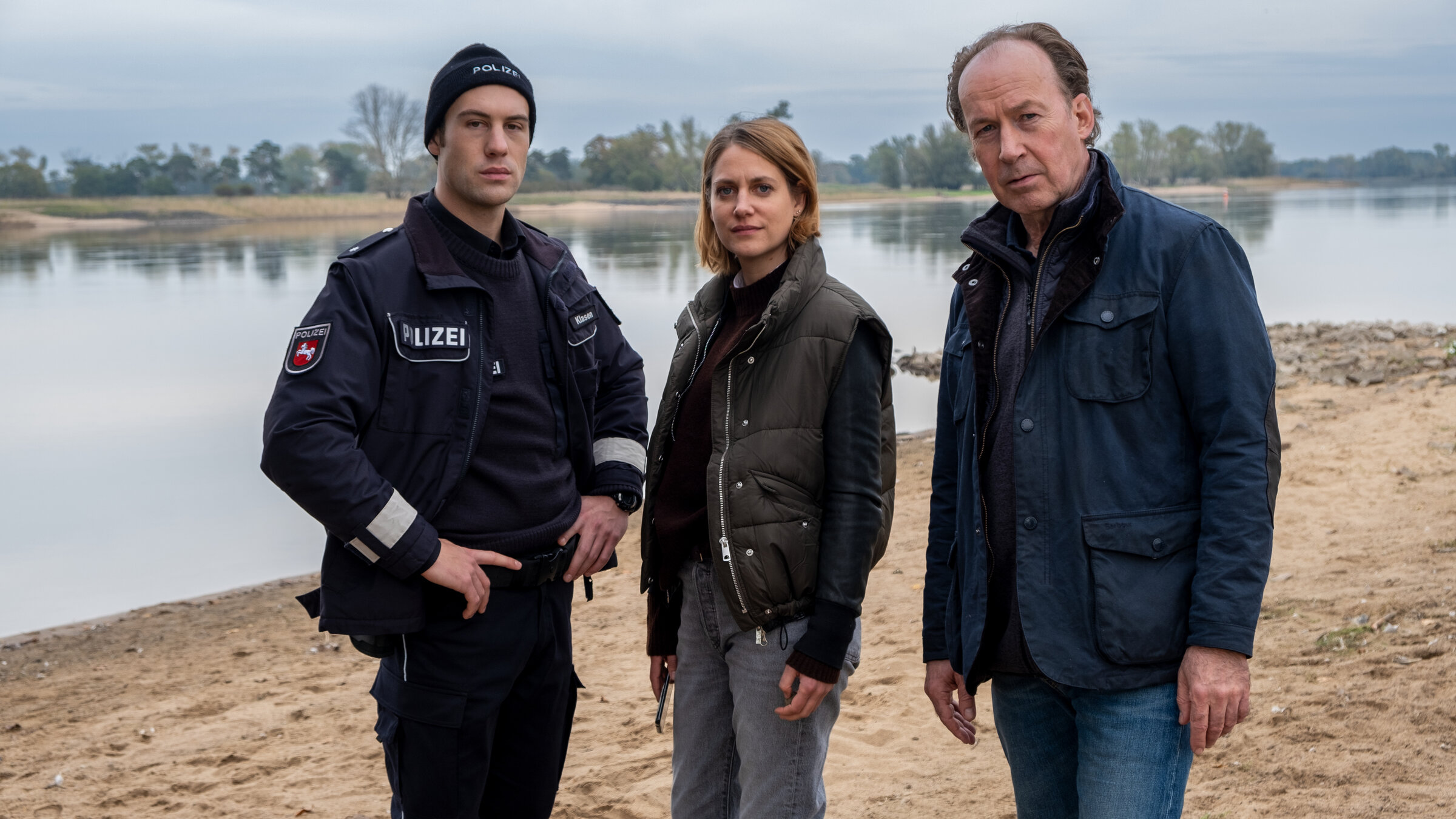 "Wendland - Stiller und das große Schweigen": Oliver Klasen (Malte Thomsen), Kira Engelmann (Bettina Burchard) und Jakob Stiller (Ulrich Noethen) stehen zusammen am Ufer.