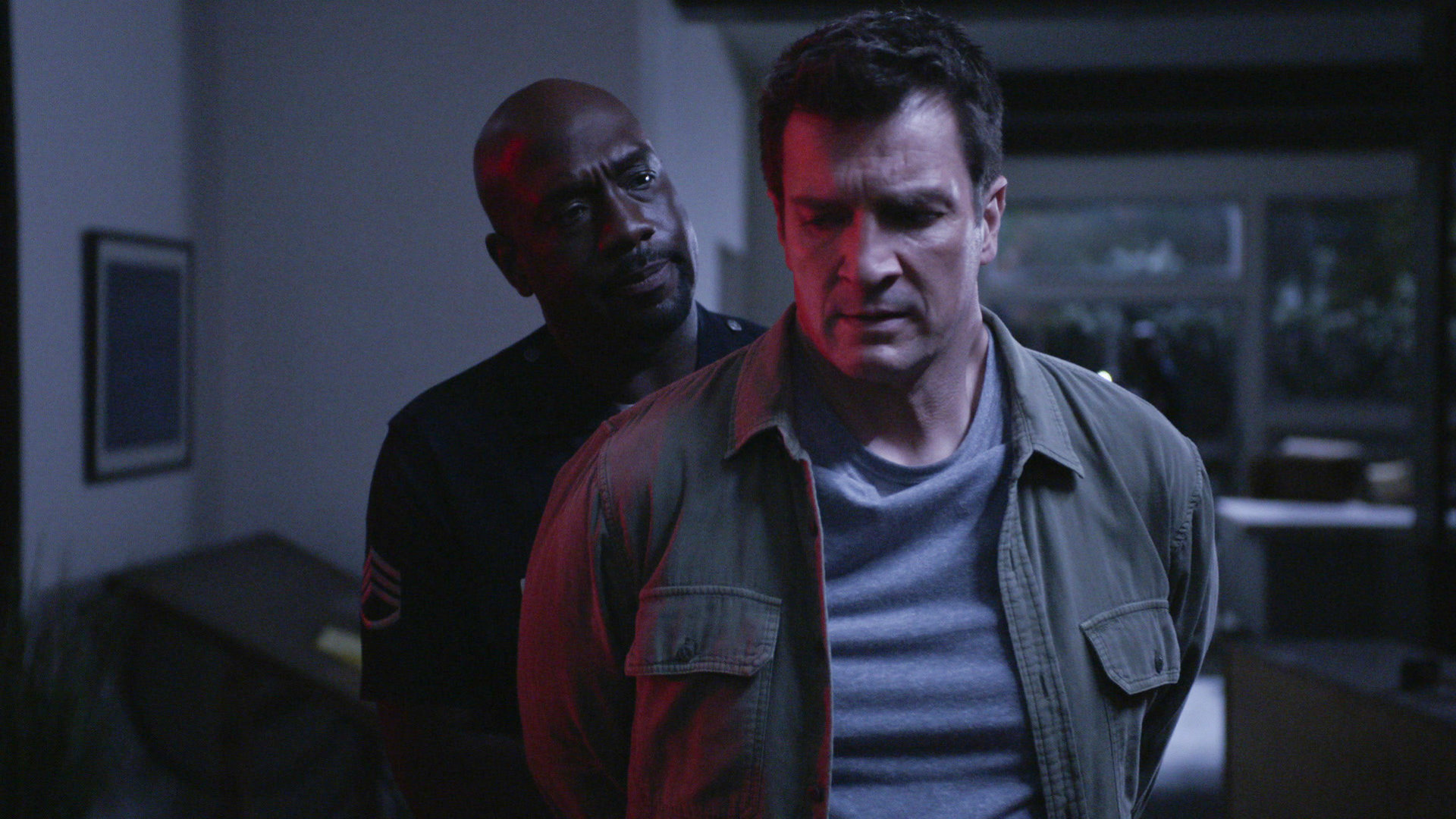 "The Rookie - Abwärts": Nolan (Nathan Fillion) steht mit den Armen hinter seinem Rücken vor Sergeant Grey (Richard T. Jones), der Nolan Handschellen umlegt und ihn dabei ernst anschaut.