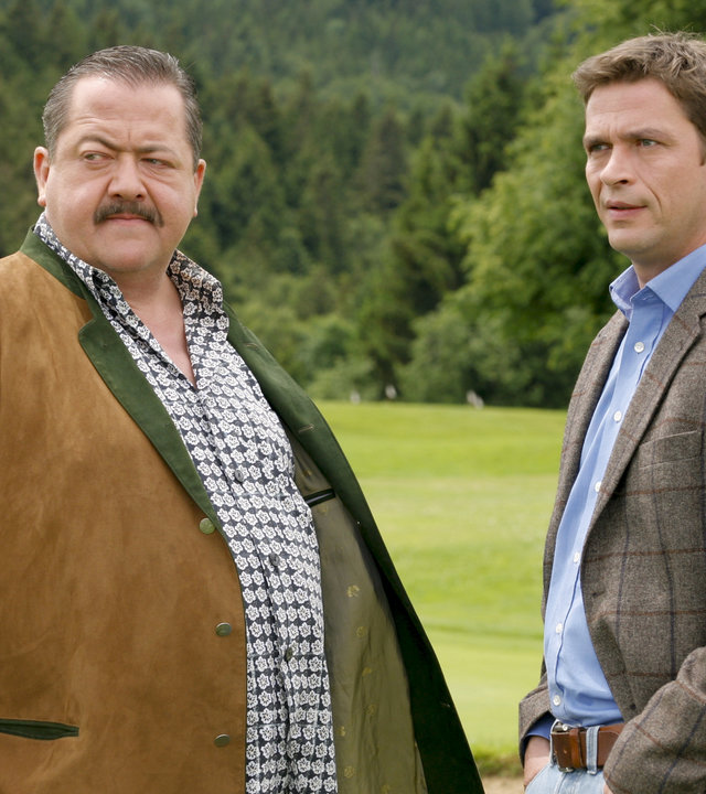 "Die Rosenheim-Cops - Ottos letzter Sieg": Die Rosenheim-Cops Korbinian Hofer (Joseph Hannesschläger) und Christian Lind (Tom Mikulla) stehen im Grünen und schauen kritisch in eine Richtung. Im Hintergrund sind viele Bäume zu sehen.