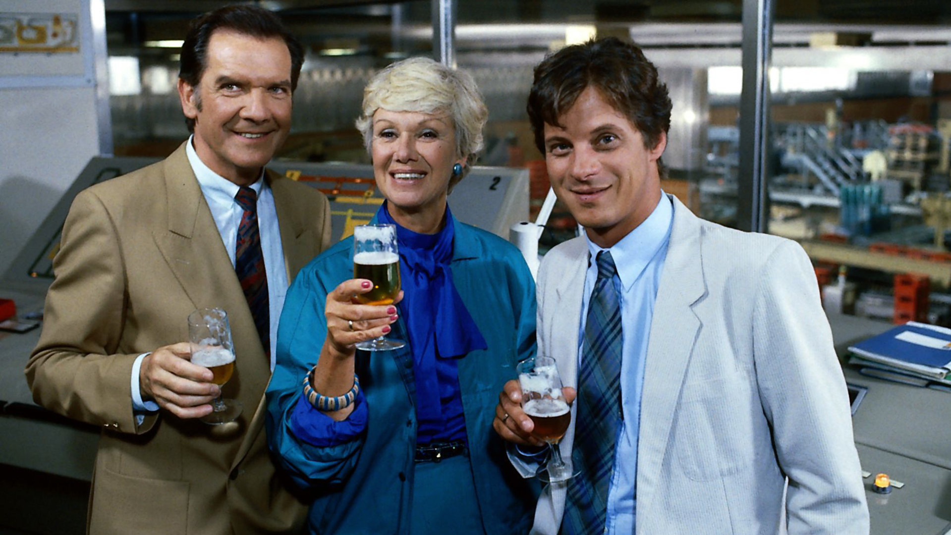 "Die Wicherts von nebenan: Die Zeit der Reife": Tenstaag (Gerhard Friedrich), Hannelore (Maria Sebaldt) und Rüdiger (Jochen Schroeder) stehen nebeneinander in der Werkstatt und halten ihre gefüllten Biergläser vor sich.
