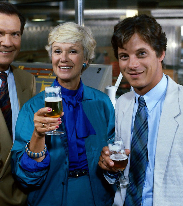 "Die Wicherts von nebenan: Die Zeit der Reife": Tenstaag (Gerhard Friedrich), Hannelore (Maria Sebaldt) und Rüdiger (Jochen Schroeder) stehen nebeneinander in der Werkstatt und halten ihre gefüllten Biergläser vor sich.