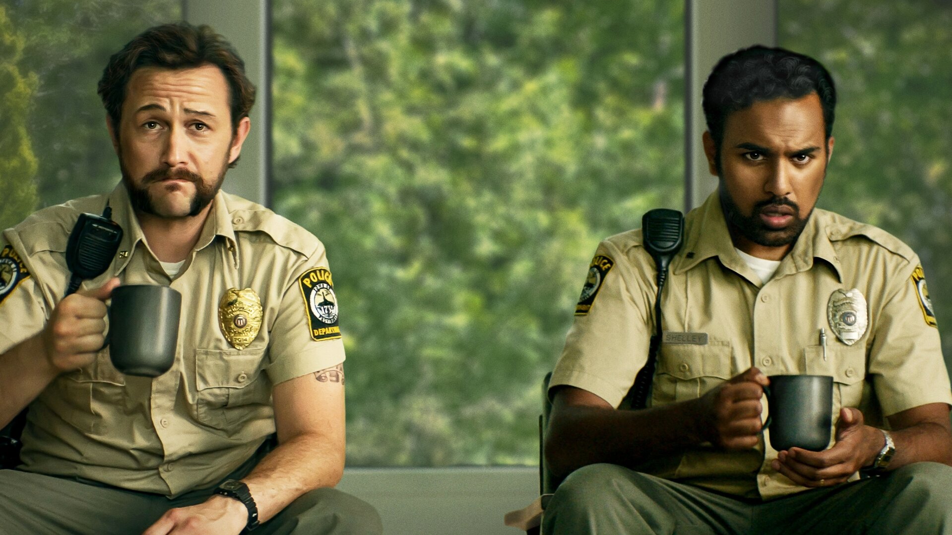 "Greedy People - Gelegenheit macht gierig": Plakatmotiv, Halbnahe: Terry (Joseph Gordon-Levitt) und Will (Himesh Patel) sitzen in Polizeiuniform nebeneinander vor einer Fensterfront mit Blick ins Grüne. Während Terry stoisch nach vorne blickt, zeigt Will einen besorgten Gesichtsausdruck. Beide halten eine Kaffeetasse in der Hand.