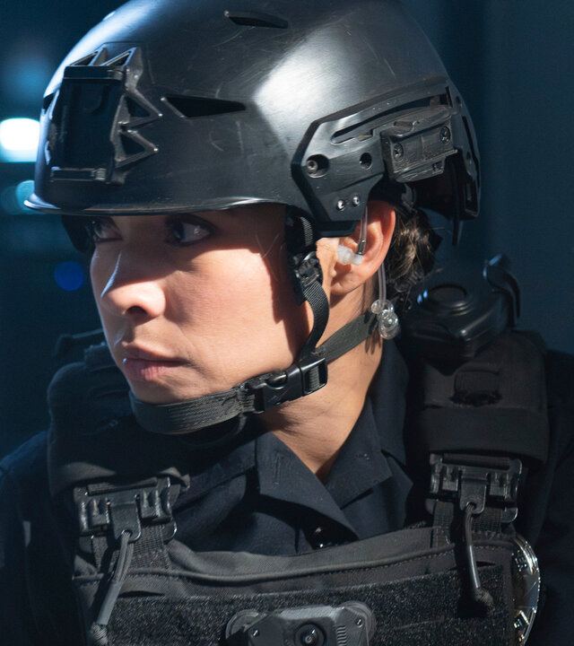 "The Rookie - April, April": Celina Juarez (Lisseth Chavez) steht in einem abgedunkelten Raum und trägt eine kugelsichere Weste sowie einen schwarzen Helm. In der Hand hält sie eine Pistole und blickt konzentriert nach vorn.