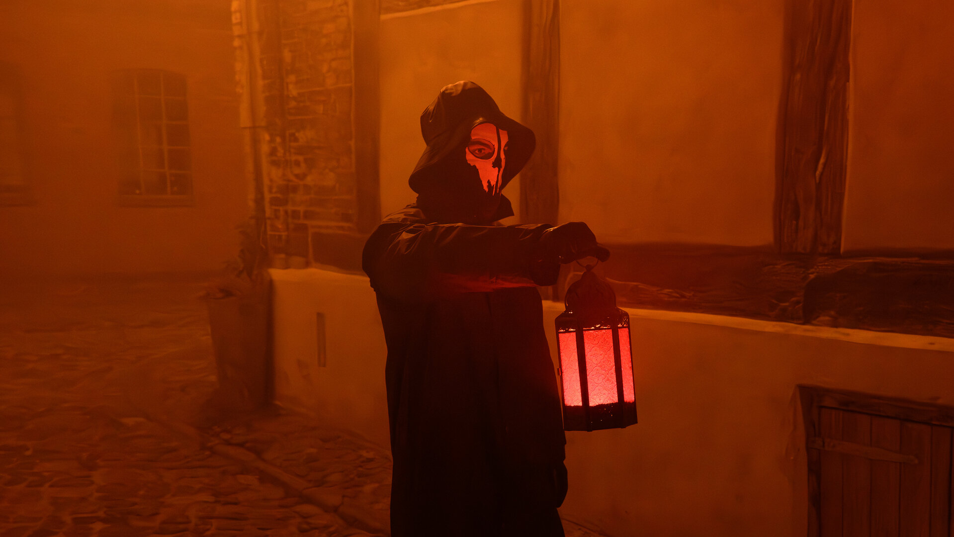 „SOKO Wismar – Der Blüser von Rerik“: In einer Gasse der Wismarer Altstadt steht eine dunkel gekleidete Gestalt, deren Gesicht von einer weißen Geistermaske verdeckt wird. In der erhobenen Hand hält sie eine Laterne, die die nächtliche Gasse in ein rötliches Licht taucht.