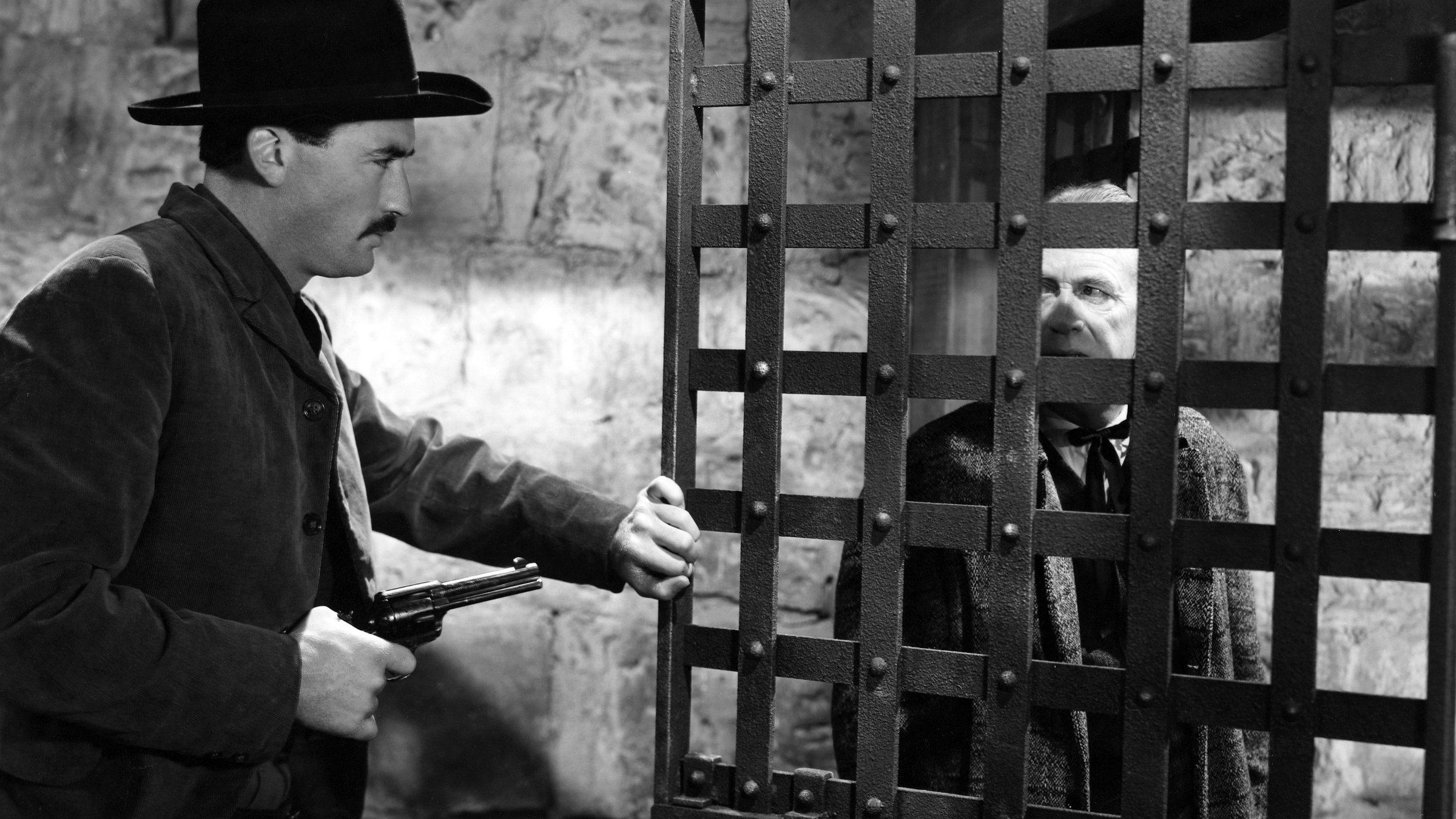 "Der Scharfschütze": Jimmy Ringo (Gregory Peck) hat einen Revolver in der Hand und schließt eine schwere Eisengittertür einer Gefängniszelle, in der ein alter Mann (Schauspieler ungenannt) steht.