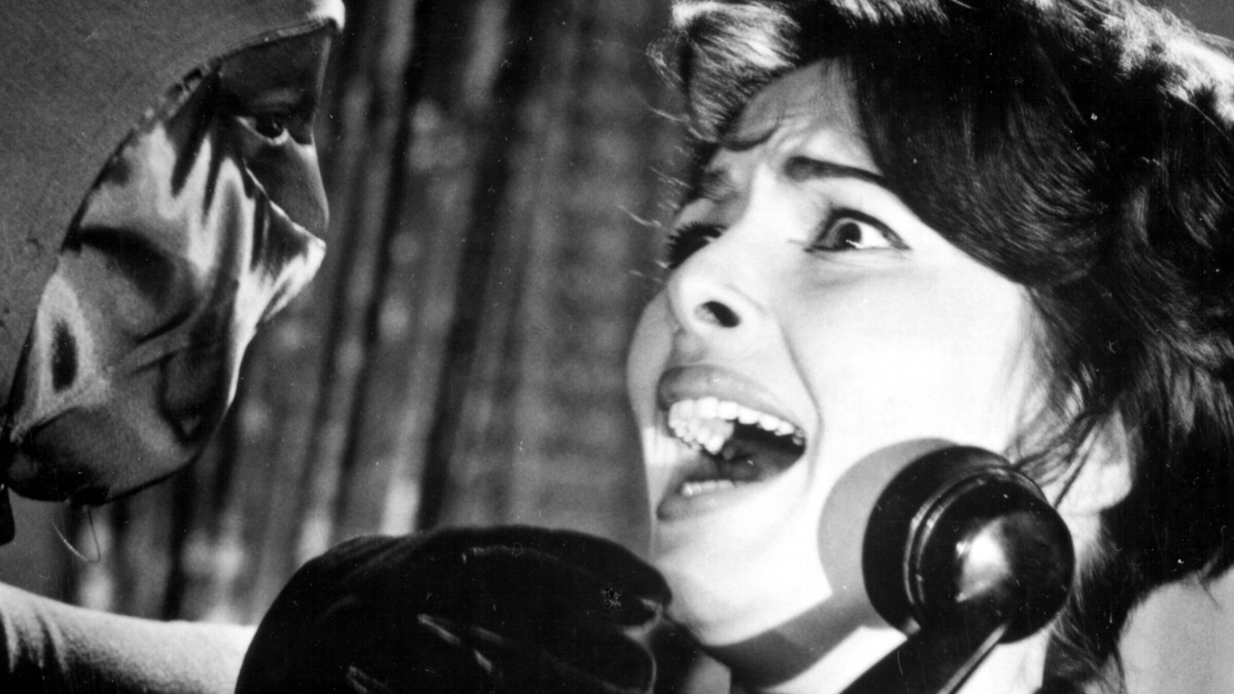 „Edgar Wallace: Der grüne Bogenschütze“: Valerie Howett (Karin Dor) schaut in Großaufnahme mit angsterfülltem Blick eine maskierte Person ihr gegenüber an, während sie einen Telefonhörer in der Hand hält.