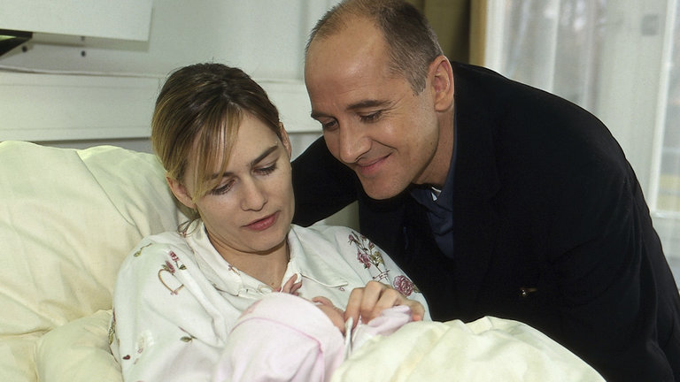 "Der letzte Zeuge - Im Schatten stirbt man nicht": Robert Kolmaar (Ulrich Mühe) steht lächelnd neben Judith (Gesine Cukrowski), die mit einem Säugling auf dem Arm im Krankenbett liegt.