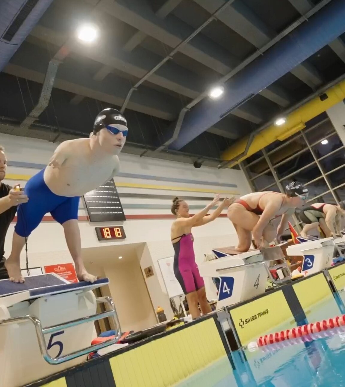 "einfach Mensch - Josia Topf: Schwimmer gegen alle Widerstände (4)": Im Schimmbad: Josia Topf startet bei einem Schwimmwettkampf mit einem Sprung vom Startblock ins Wasser. Im Hintergrund starten zwei weitere Schimmer.