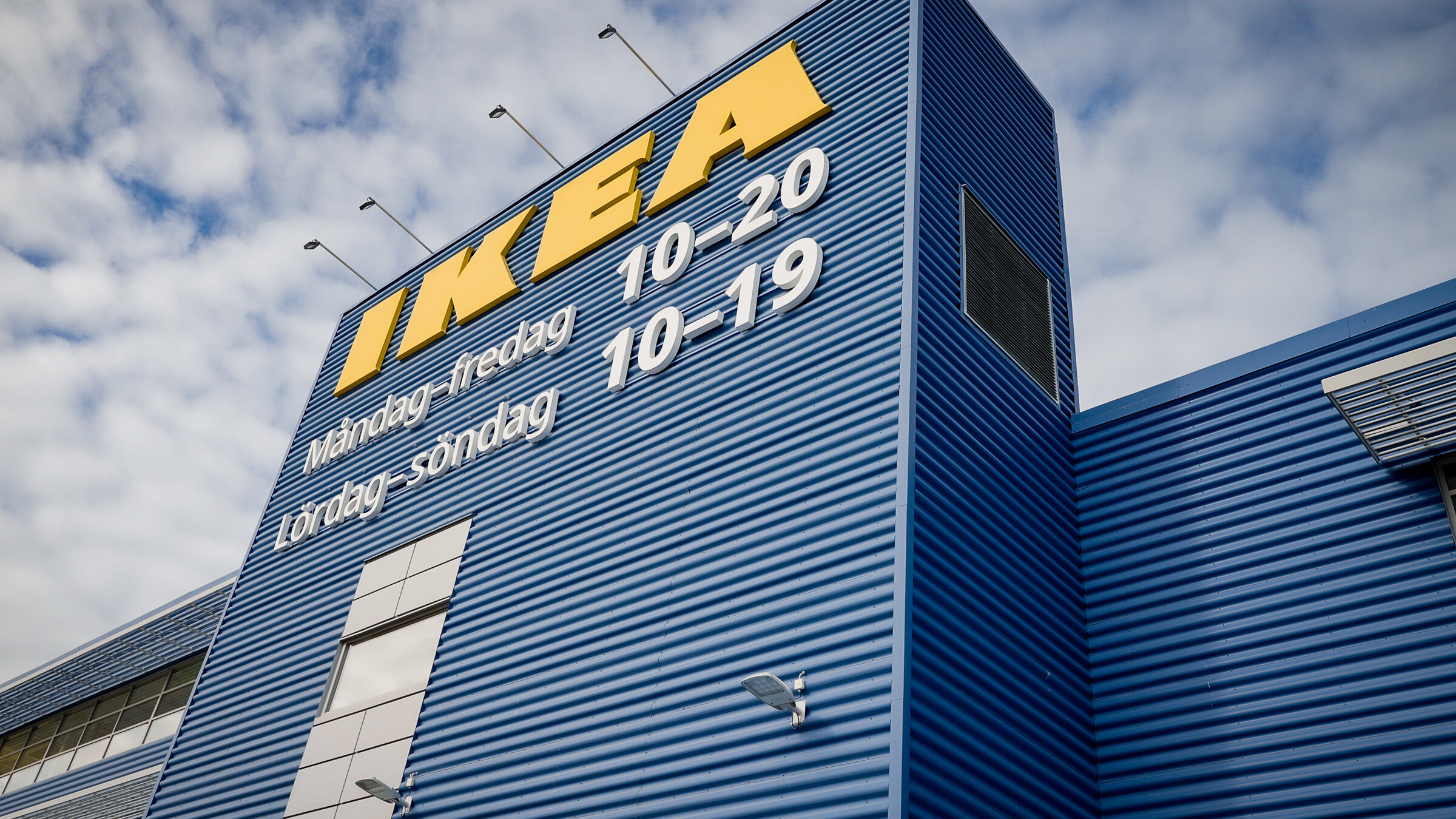 "Greenwashed? - IKEA und Nachhaltigkeit - Woher stammt das Holz für die Möbel?": Blick von unten auf die blau gestrichene Fassade einer IKEA-Filiale. Man sieht den Schriftzug "IKEA" in riesigen gelben Lettern sowie die Öffnungszeiten auf Schwedisch.