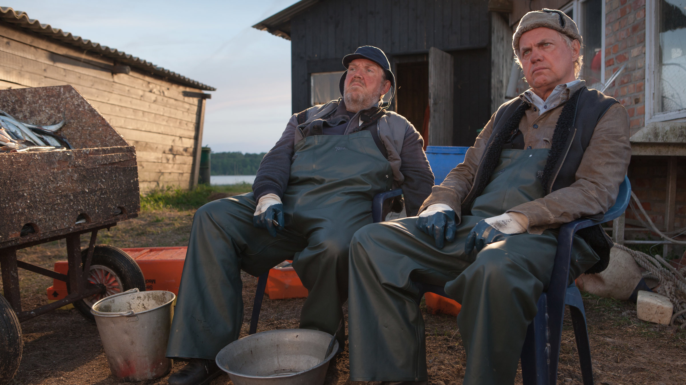 "Große Fische, kleine Fische": Paul (Uwe Ochsenknecht) und Fiete (Dietmar Bär) sitzen zusammen in Fischerkleidung auf einer Bank. Vor ihnen leere Eimer.