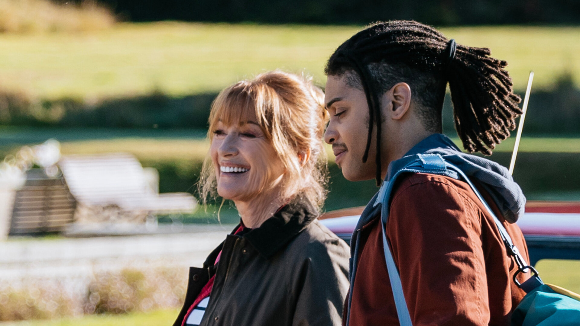 "Harry Wild – Mörderjagd in Dublin - Ein Hochzeits-Crasher aus der Hölle (1)": Harry Wild (Jane Seymour) und Fergus Reid (Rohan Nedd) stehen im Freien vor einem Auto. Bei wirken sehr gut gelaunt. Fergus trägt eine große Umhängetasche über der rechten Schulter.