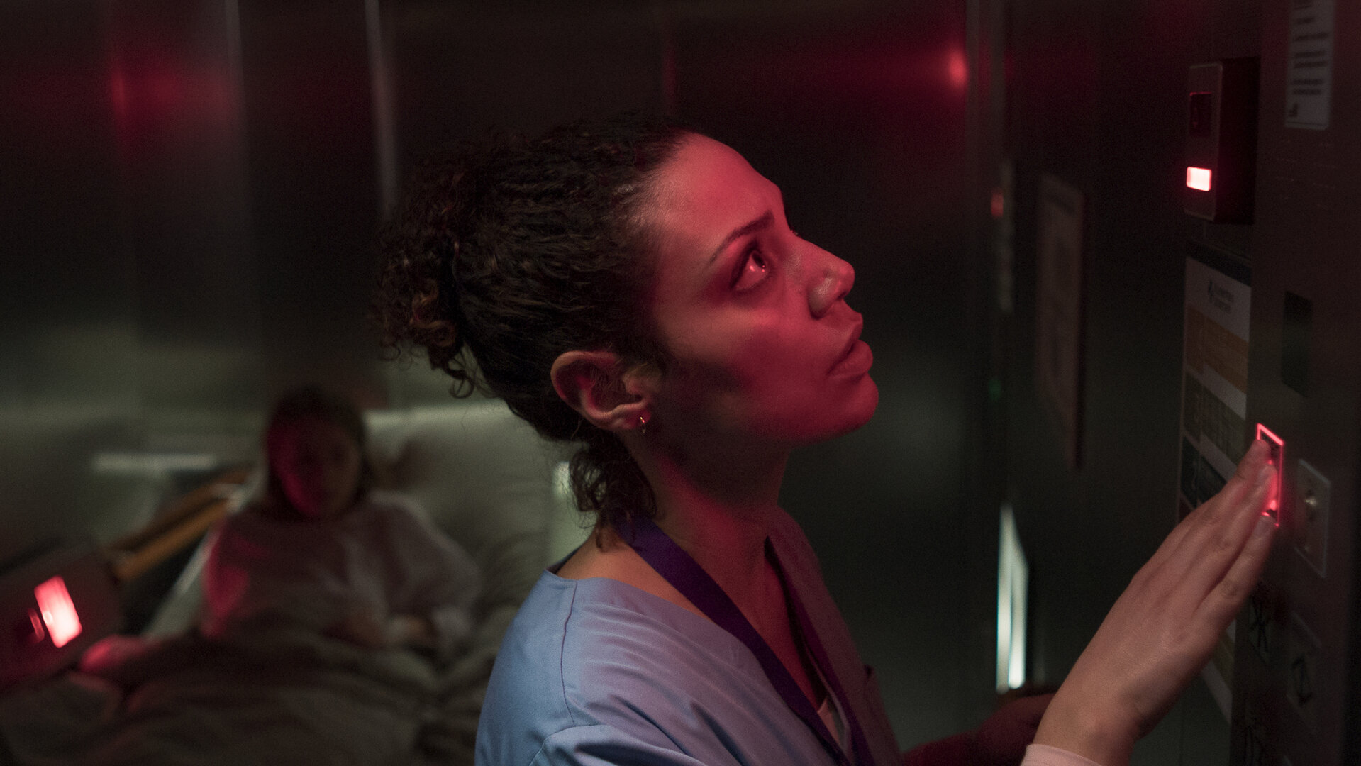 "Doktor Ballouz - Gesprächsbedarf": Schwester Carla (Haley Louise Jones) steht in einem dunklen Fahrstuhl vor dem Bedienelement. Hinter ihr liegt die Patientin Anja (Anna Brüggemann) auf eine Liege.