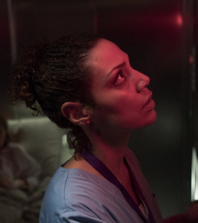 "Doktor Ballouz - Gesprächsbedarf": Schwester Carla (Haley Louise Jones) steht in einem dunklen Fahrstuhl vor dem Bedienelement. Hinter ihr liegt die Patientin Anja (Anna Brüggemann) auf eine Liege.