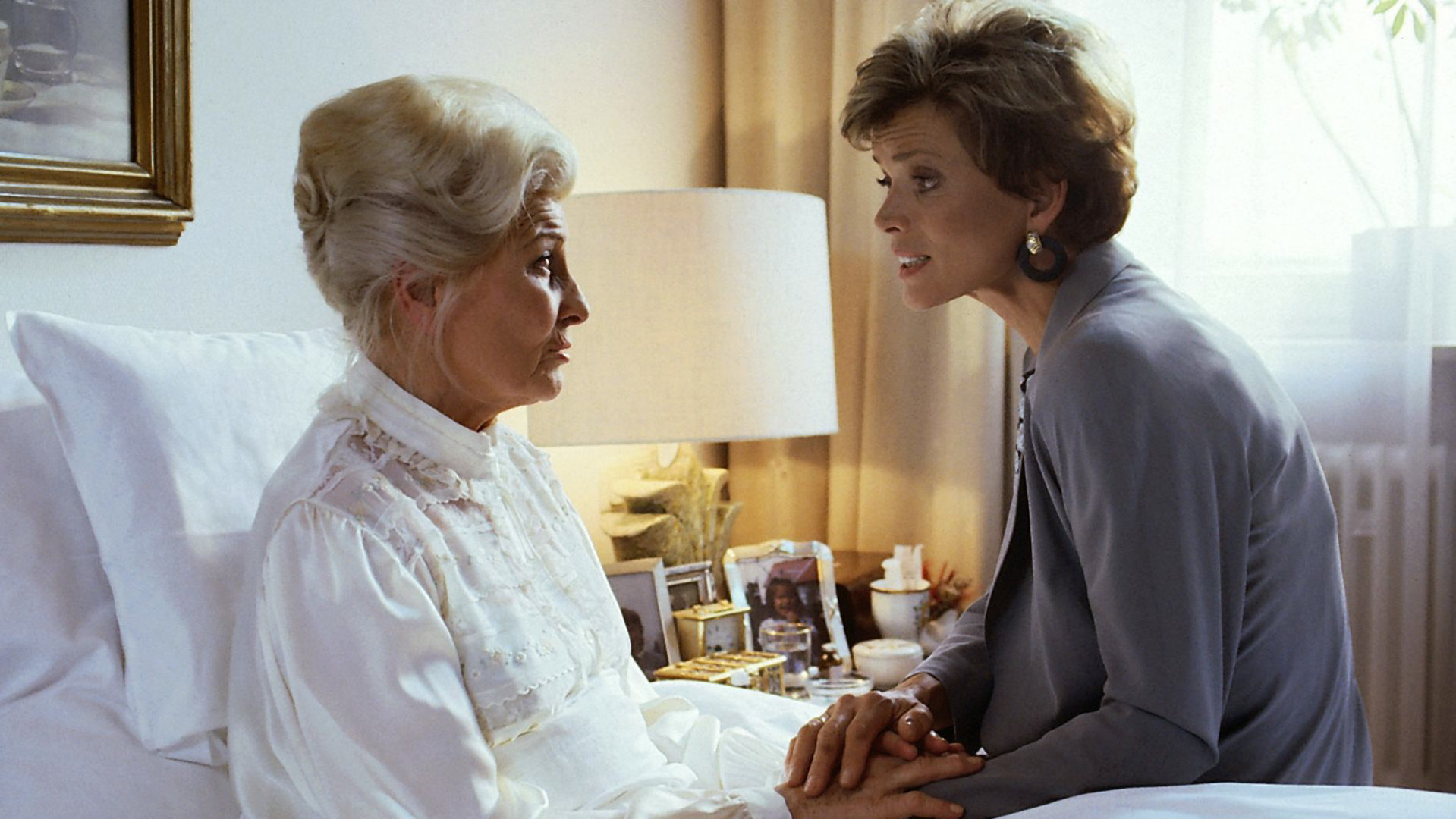 "Zwei Münchner in Hamburg - Tizian, der Wundertraber": Julia (Uschi Glas) besucht ihre Mutter Hermine (Winnie Markus). Hermine sitzt in ihrem Bett, Julia sitzt daneben und hält ihre Hand.