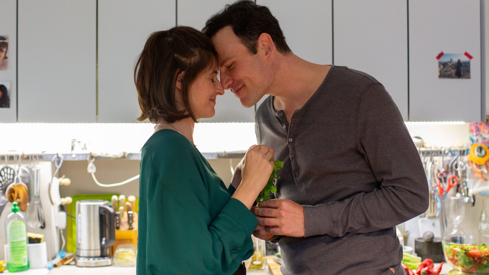 "Letzte Spur Berlin - Amöbenliebe": Christoph (Peter Becker) und Annika (Eva Bay) stehen in einer Küche nah beieinander. Christoph hat sich zu Annika gebeugt und seine Stirn an ihre gelehnt. Beide haben die Augen geschlossen und lächeln.
