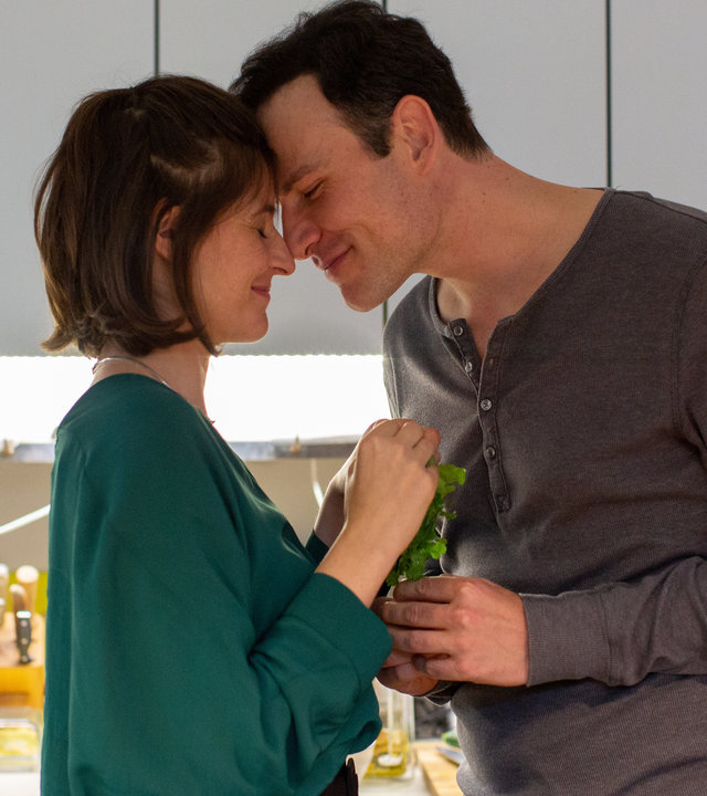 "Letzte Spur Berlin - Amöbenliebe": Christoph (Peter Becker) und Annika (Eva Bay) stehen in einer Küche nah beieinander. Christoph hat sich zu Annika gebeugt und seine Stirn an ihre gelehnt. Beide haben die Augen geschlossen und lächeln.