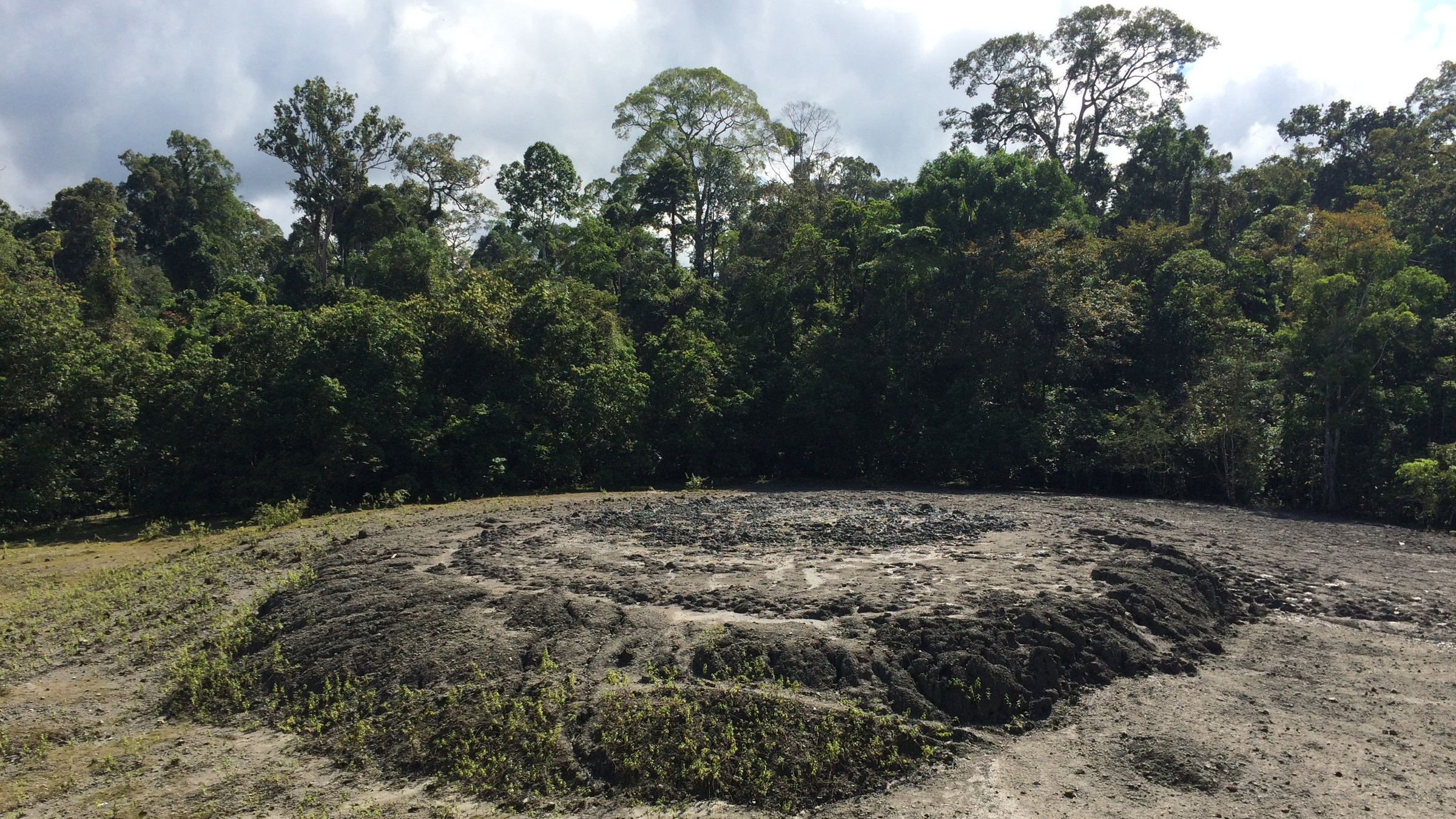 "Indonesien - ungezähmt: Im Schatten der Vulkane": Eine karge Landschaft mit kleiner runder Erhebung. Im Hintergrund ist Wald zu sehen.