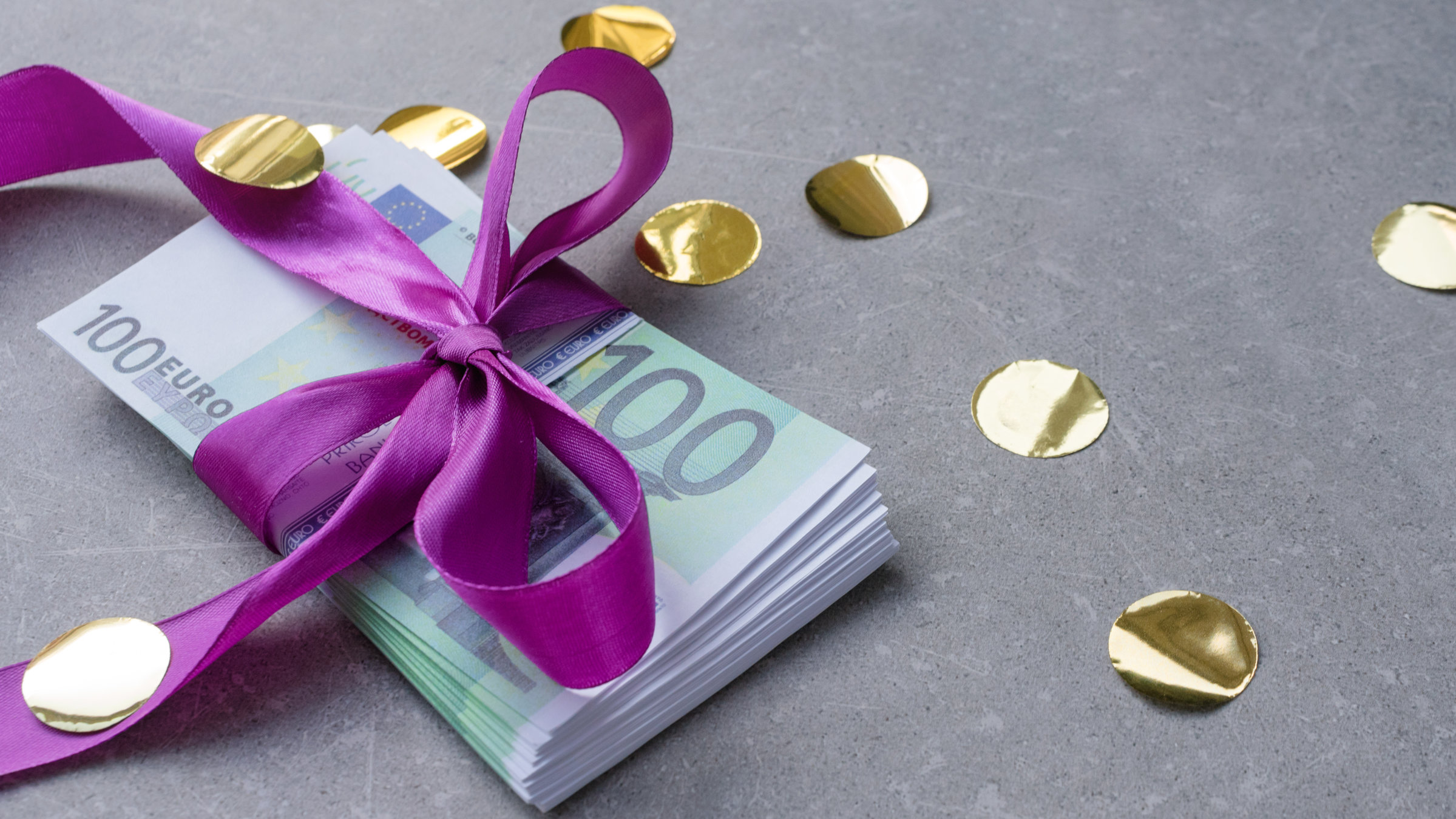 "WISO-Dokumentation: Ein Erbe vom Staat? 20.000 Euro für Jeden":  Ein Stapel 100-Euro-Scheine mit einer lila Schleife liegt auf einem grauen Untergrund.