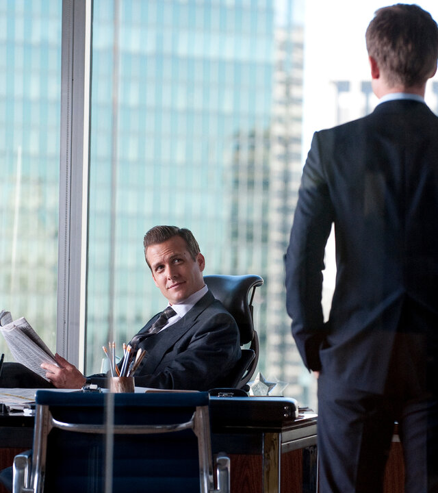 "Suits - Doppeltes Spiel": Harvey Specter (Gabriel Macht) sitzt entspannt mit hochgelegten Füßen an seinem Schreibtisch und blickt Mike Ross (Patrick J. Adams) an, der ihm mit dem Rücken zur Kamera gegenübersteht. Im Hintergrund geben große Fenster den Blick auf die Skyline frei.