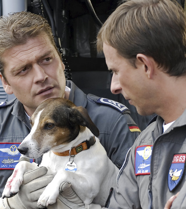 "Die Rettungsflieger - Mitten im Leben": Wollcke (Oliver Hörner) und Blank (Nicolas König) stehen vor dem Hubschrauber. Wollcke hält den kleinen verletzten Hund Percy auf seinem Arm.