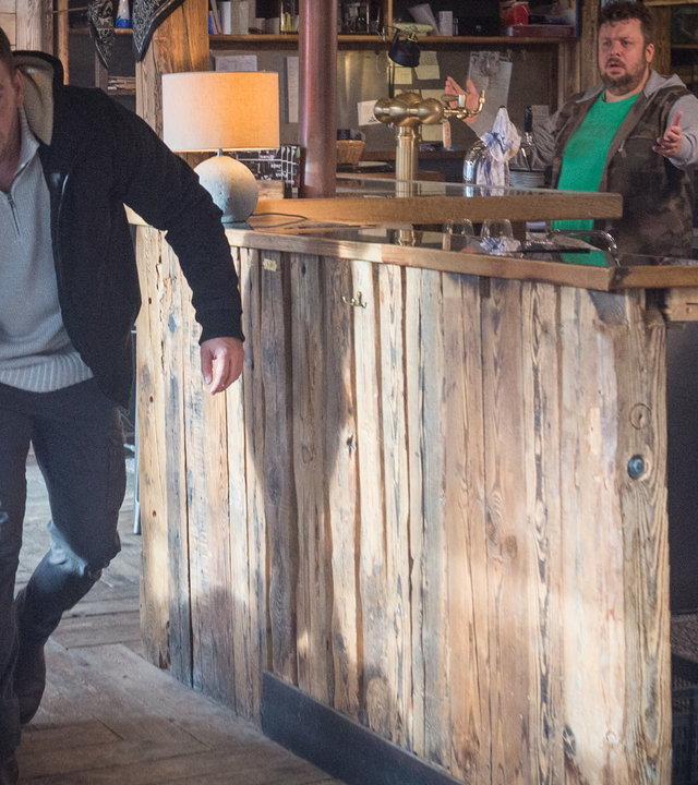 "SOKO Wismar – Schlafende Hunde": In einer Gaststätte greift Lars Pöhlmann (Dominic Boeer) gebückt nach einem Rottweiler und führt ihn hinaus. Der Wirt Arne Weiss (Till Butterbach), der hinterm Tresen steht, sieht Lars und dem Rottweiler aufgebracht hinterher.