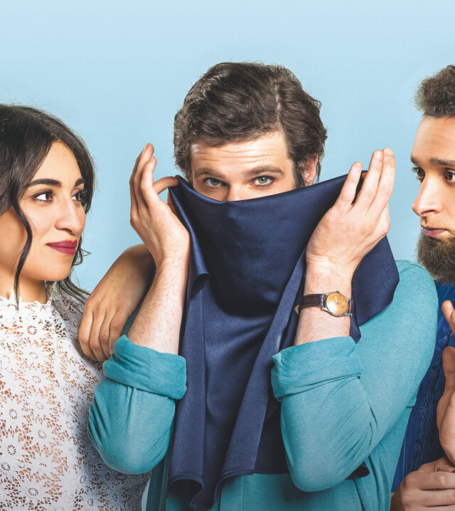 "Voll verschleiert": Leila (Cámelia Jordana), Armand (Félix Moati) und Mahmoud (William Lebghil) stehen nebeneinander vor einem hellblauen Hintergrund. Leila und Mahmoud, der ein dunkelblaues Gewand trägt, stehen links und rechts von Armand und blicken ihn an. Armand steht in der Mitte und hält sich einen dunkelblauen Niqab vor den Mund.
