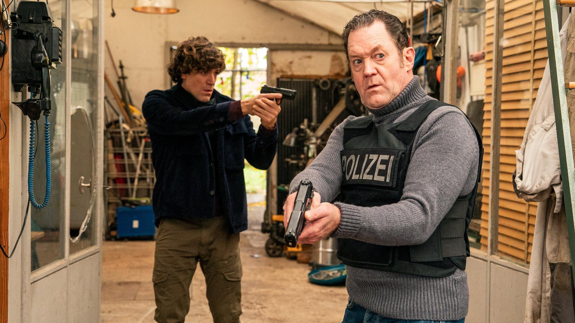 "Die Chefin - Schattenkrieger": Korbinian Kirchner (Jonathan Hutter, l.) und Paul Böhmer (Jürgen Tonkel, r.) bewegen sich vorsichtig und mit gezogener Waffe durch ein geräumiges Gartenhaus. Böhmer trägt eine kugelsichere Weste. Im Hintergrund stehen allerlei Gerätschaften herum.