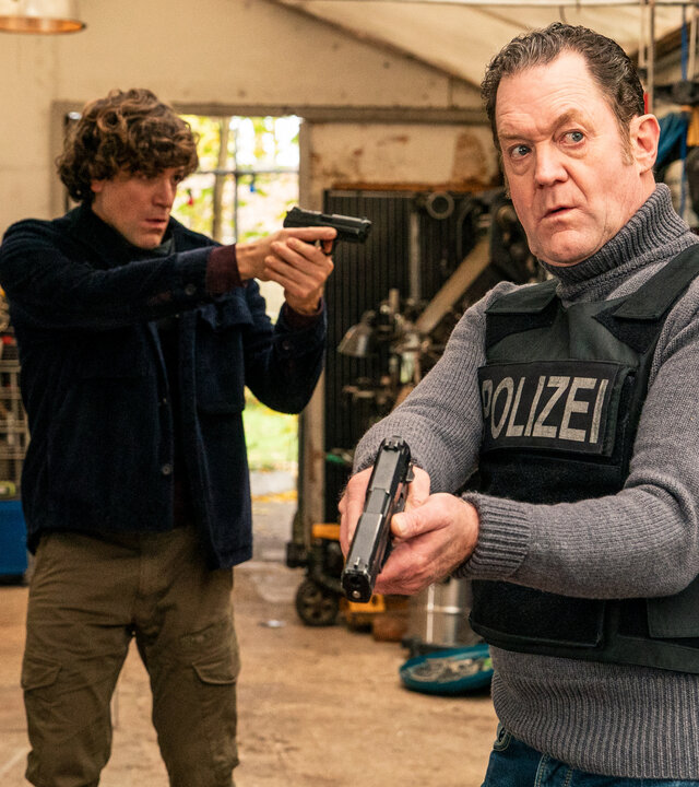 "Die Chefin - Schattenkrieger": Korbinian Kirchner (Jonathan Hutter, l.) und Paul Böhmer (Jürgen Tonkel, r.) bewegen sich vorsichtig und mit gezogener Waffe durch ein geräumiges Gartenhaus. Böhmer trägt eine kugelsichere Weste. Im Hintergrund stehen allerlei Gerätschaften herum.