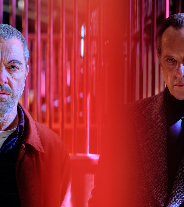 "Suspect - Folge 6: Harry": Danny (James Nesbitt) und Harry Carr (Richard E. Grant) stehen nebeneinander vor den Pferdeboxen auf der Rennbahn.