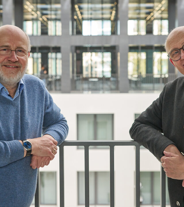 "Lesch sieht Schwartz: Solidarisch sein - was bringt's?": Harald Lesch und Thomas Schwartz stehen hoch oben in einem modernen Hochhaus vor einem Innenhof und lächeln in die Kamera.