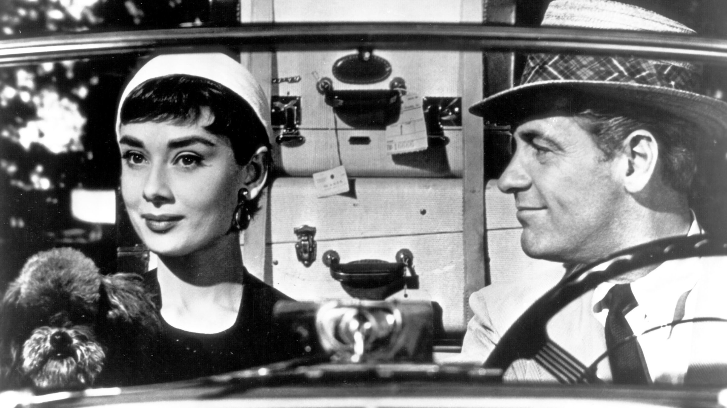 "Sabrina": Im Auto von vorn: Sabrina Fairchild (Audrey Hepburn) schaut lächelnd in die Ferne, während David Larrabee (William Holden) sie amüsiert von der Seite ansieht.
